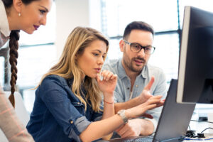 Zwei Frauen und ein Mann diskutieren am Laptop im Büro