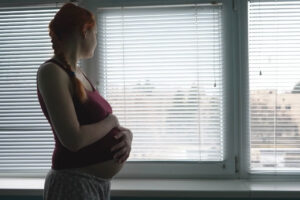 Schwangere Frau hat Angst vor einem Kaiserschnitt und blickt sorgenvoll aus dem Fenster.