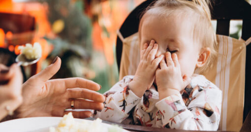 Kleinkind sitzt im Restaurant beim Essen und hält sich die Hände vor das Gesicht.
