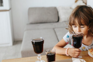 Kind hält Glas mit Cola in der Hand und trinkt daraus.