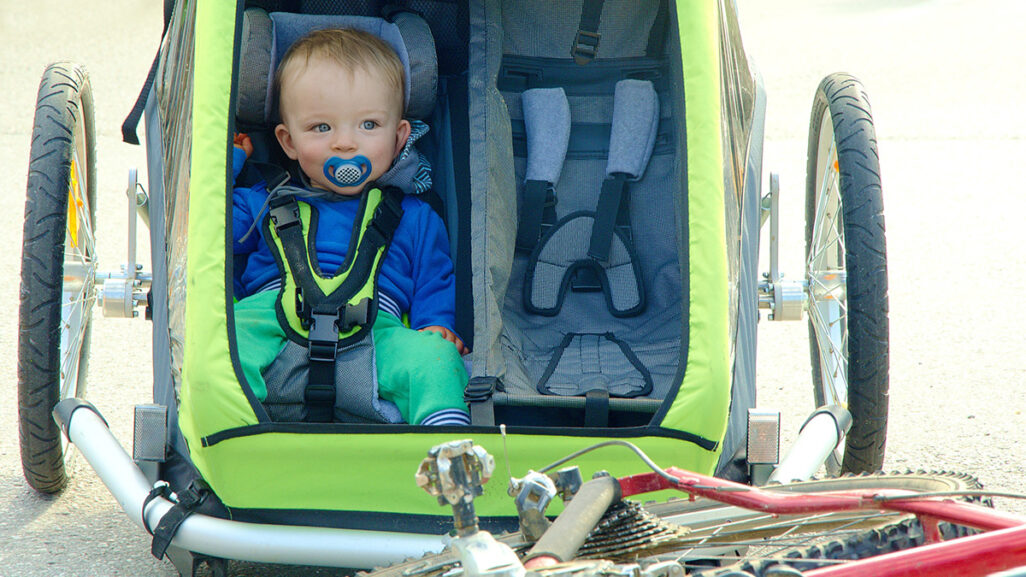 Ein Baby sitzt angeschnallt in einem stehenden Fahrradanhänger.