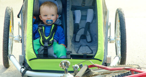 Ein Baby sitzt angeschnallt in einem stehenden Fahrradanhänger.