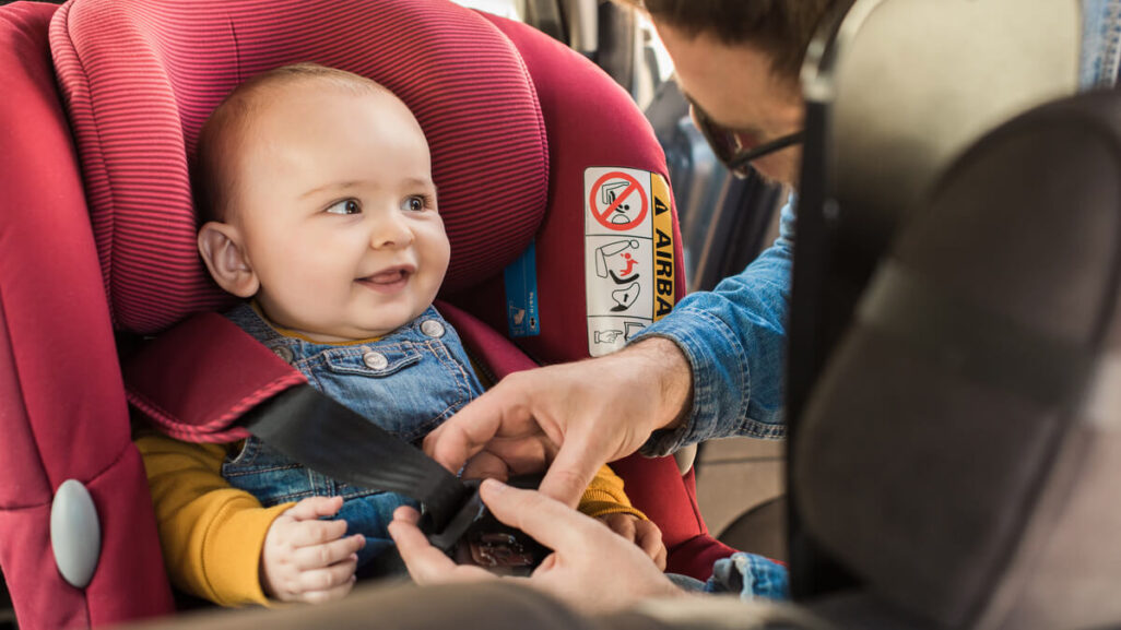 Vater schließt den Sicherheitsgurt des Kindersitzes, indem das Baby im Auto sitzt.