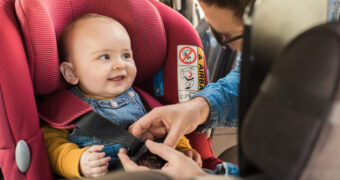 Vater schließt den Sicherheitsgurt des Kindersitzes, indem das Baby im Auto sitzt.