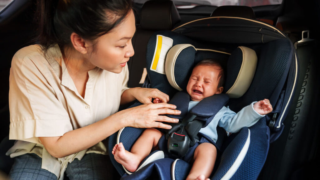 Mutter versucht weinendes Baby im Kindersitz im Auto zu beruhigen.