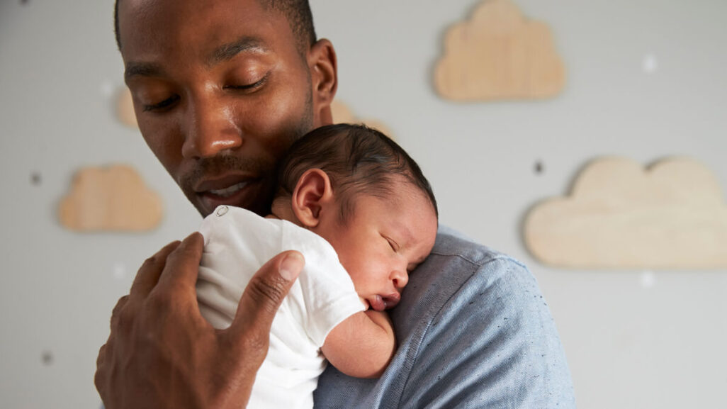 Vater kuschelt mit Baby im Stehen, während dieses einschläft.