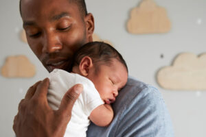 Vater kuschelt mit Baby im Stehen, während dieses einschläft.