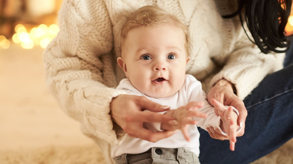 Mutter nimmt Babys Hände und klatscht damit in vorweihnachtlicher Atmosphäre.