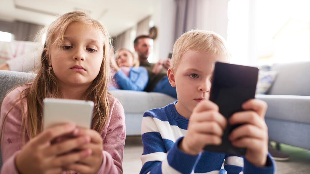 Kinder und Eltern sitzen im Wohnzimmer und schauen auf ihre Handys