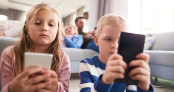 Kinder und Eltern sitzen im Wohnzimmer und schauen auf ihre Handys