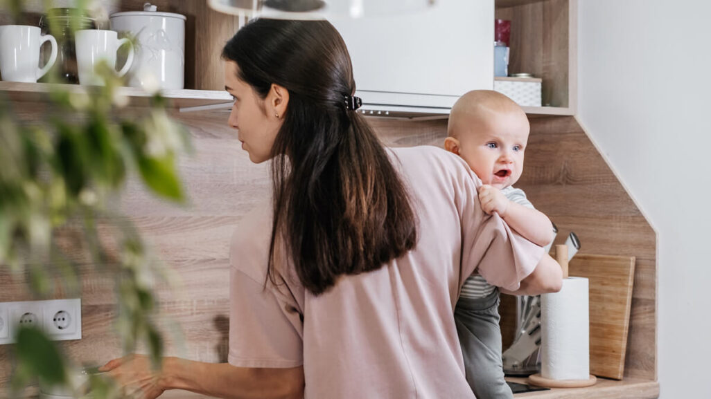 Mutter hantiert in der Küche mit Baby auf dem Arm.