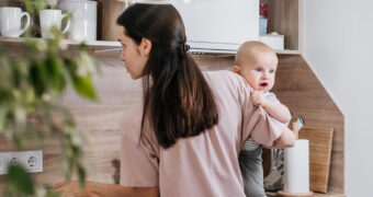 Mutter hantiert in der Küche mit Baby auf dem Arm.