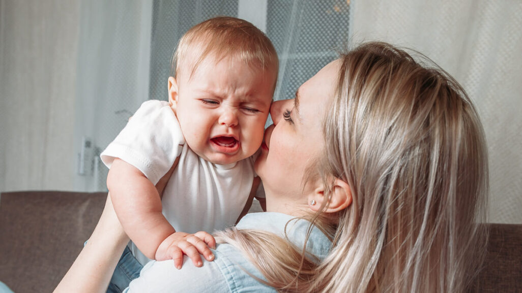 Mutter versucht mit ihrem weinenden Baby zu kuscheln.