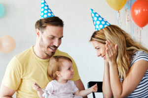 Eltern mit Partyhüten auf dem Kopf feiern zusammen mit dem Baby Geburtstag.