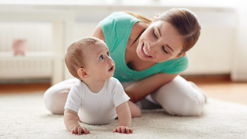 Mutter ist mit ihrem Baby auf dem Boden. Das Baby liegt in der Bauchlage.