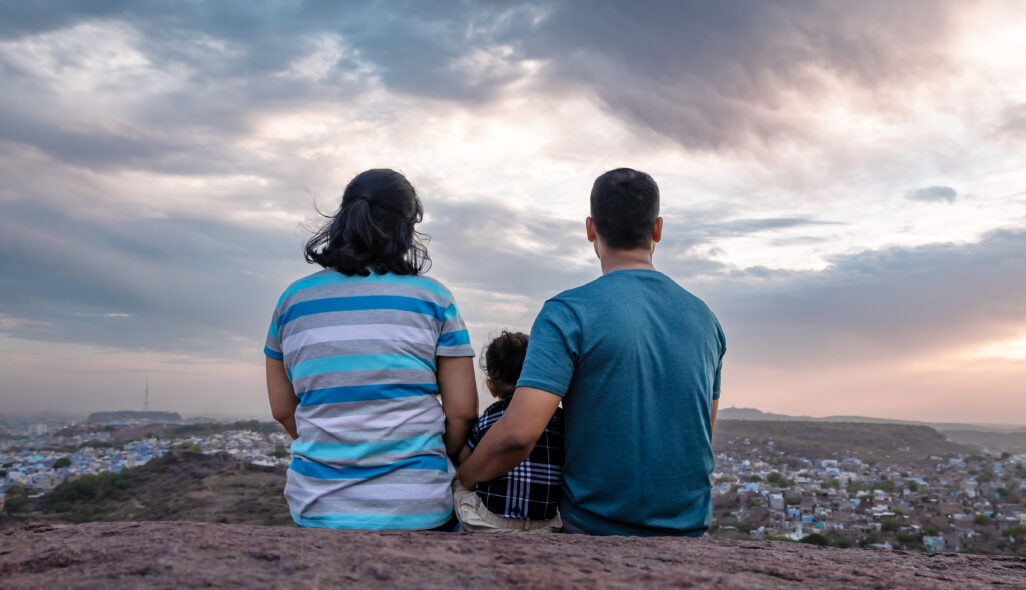 Eltern sitzen mit Kind auf einer Anhöhe und schauen runter auf eine Stadt