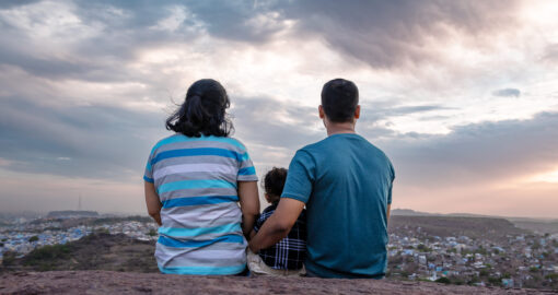 Eltern sitzen mit Kind auf einer Anhöhe und schauen runter auf eine Stadt