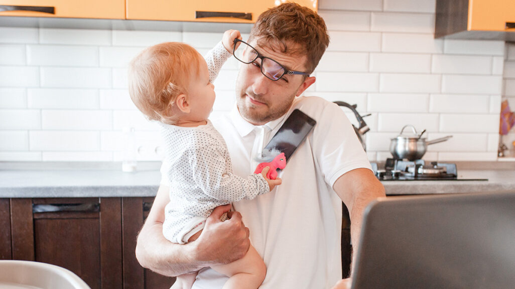 Papa am Laptop hat Baby auf dem Arm, das ihm die Brille abzieht