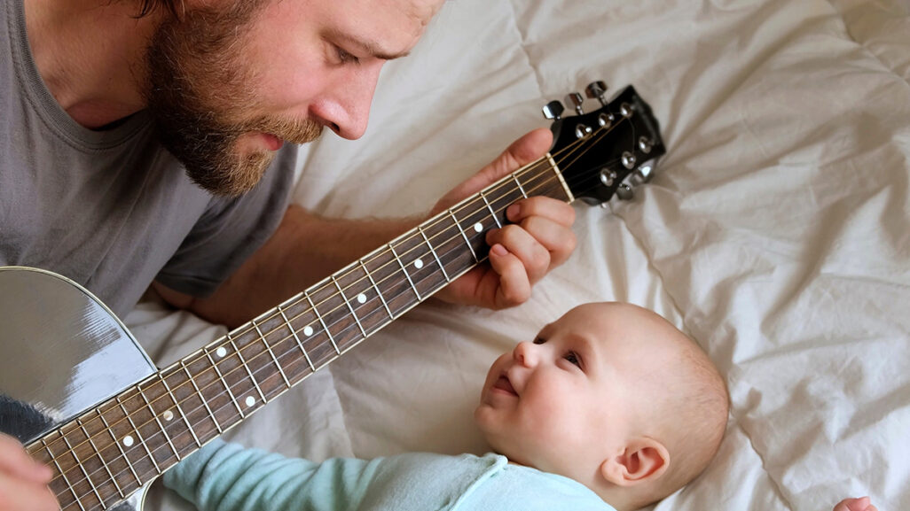 Bärtiger Vater spielt dem Baby Gitarre vor