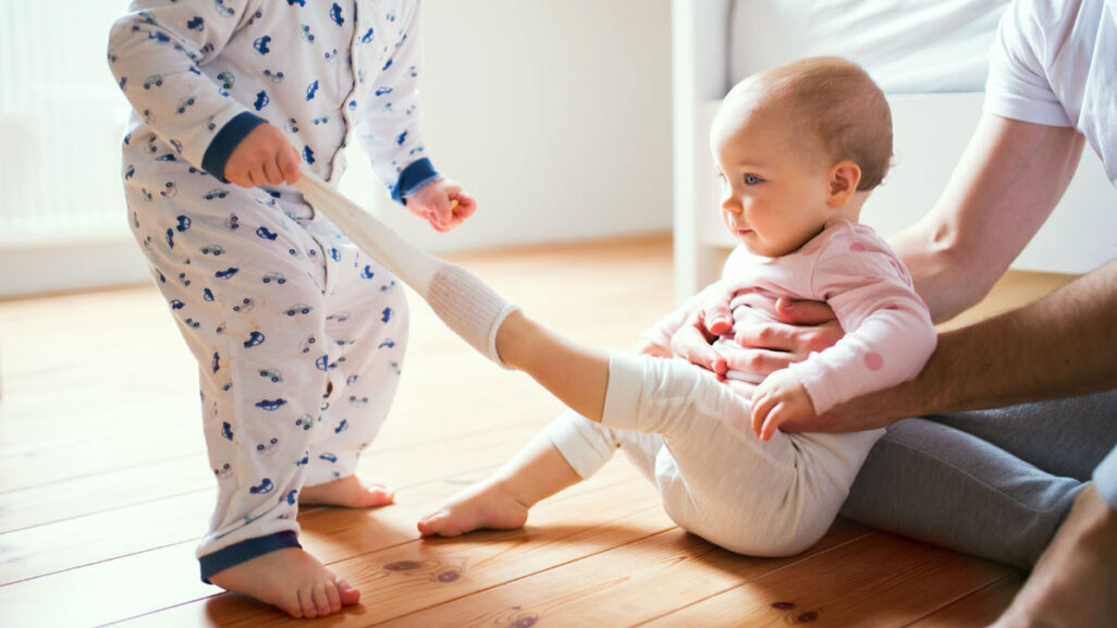 Kleinkind zieht einem Baby die Socken aus.