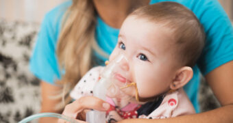 Babymädchen inhaliert Wasserdampf durch eine Maske mithilfe seiner Mutter.